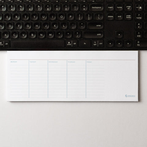Weekly planner notepad on a desk in front of a keyboard